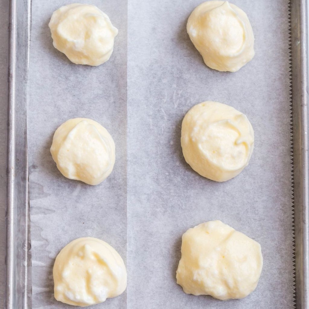 A baking sheet that is lined with parchment paper and has six scoops of cloud bread mixture ready to be baked.