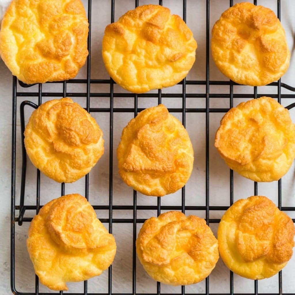 Nine pieces of baked cloud bread cooling on a black wire rack.