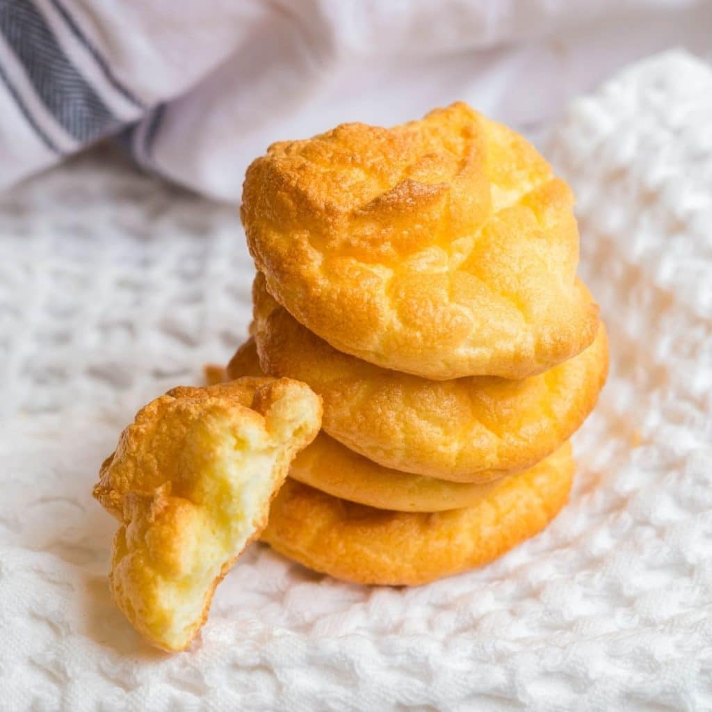 Four pieces of cloud bread stacked on top of each other with one half piece resting on the stack, and all of the cloud bread is sitting on top of a white napkin.