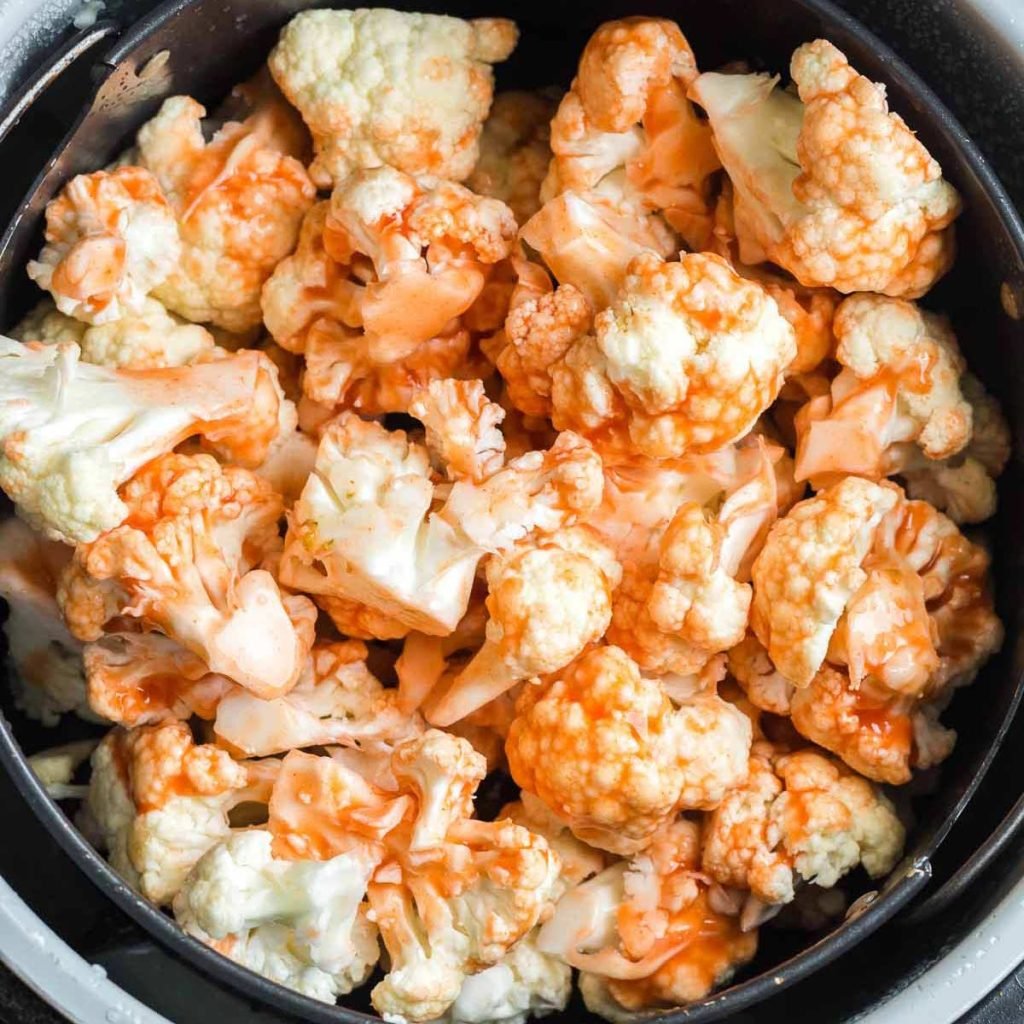 cauliflower florets inside an air fryer and tossed with hot sauce.