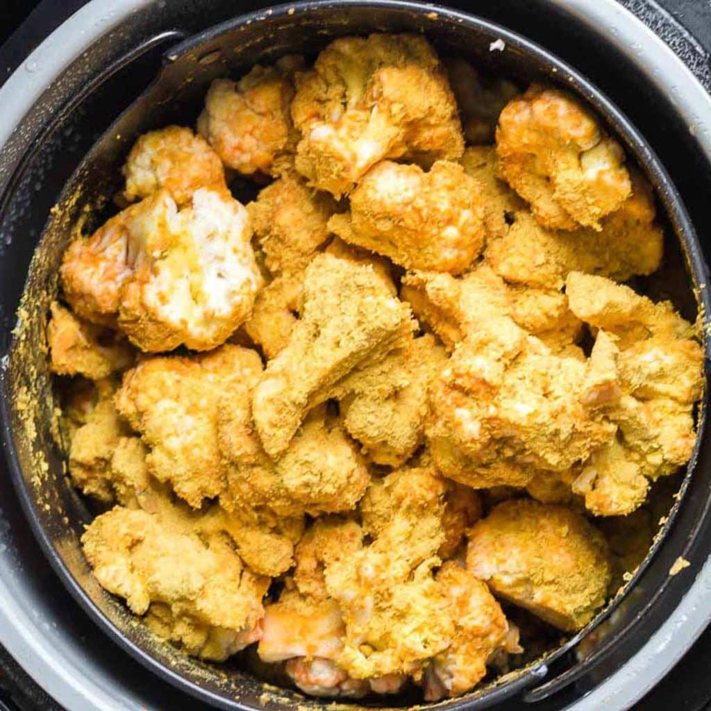 cauliflower florets in an air fryer and covered with nutritional yeast.