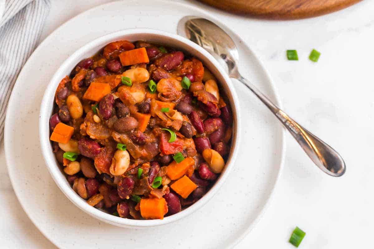 A white plate with a white bowl on top of it and filled with vegan chili.