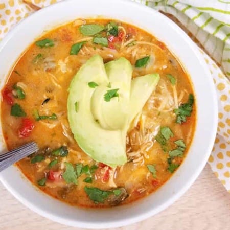 close up of cooked White Chicken Chili in a white bowl with sliced avocado on top