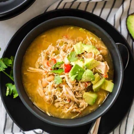 Black and white striped napkin with black bowl on top filled with white chicken chili and topped with avocado and cilantro.