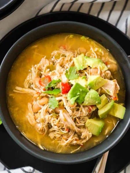 Black and white striped napkin with black bowl on top filled with white chicken chili and topped with avocado and cilantro.