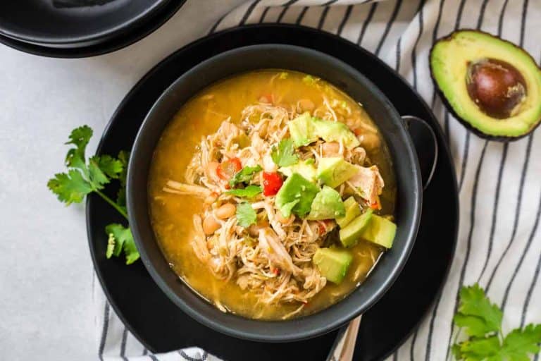 Black and white striped napkin with black bowl on top filled with white chicken chili and topped with avocado and cilantro.
