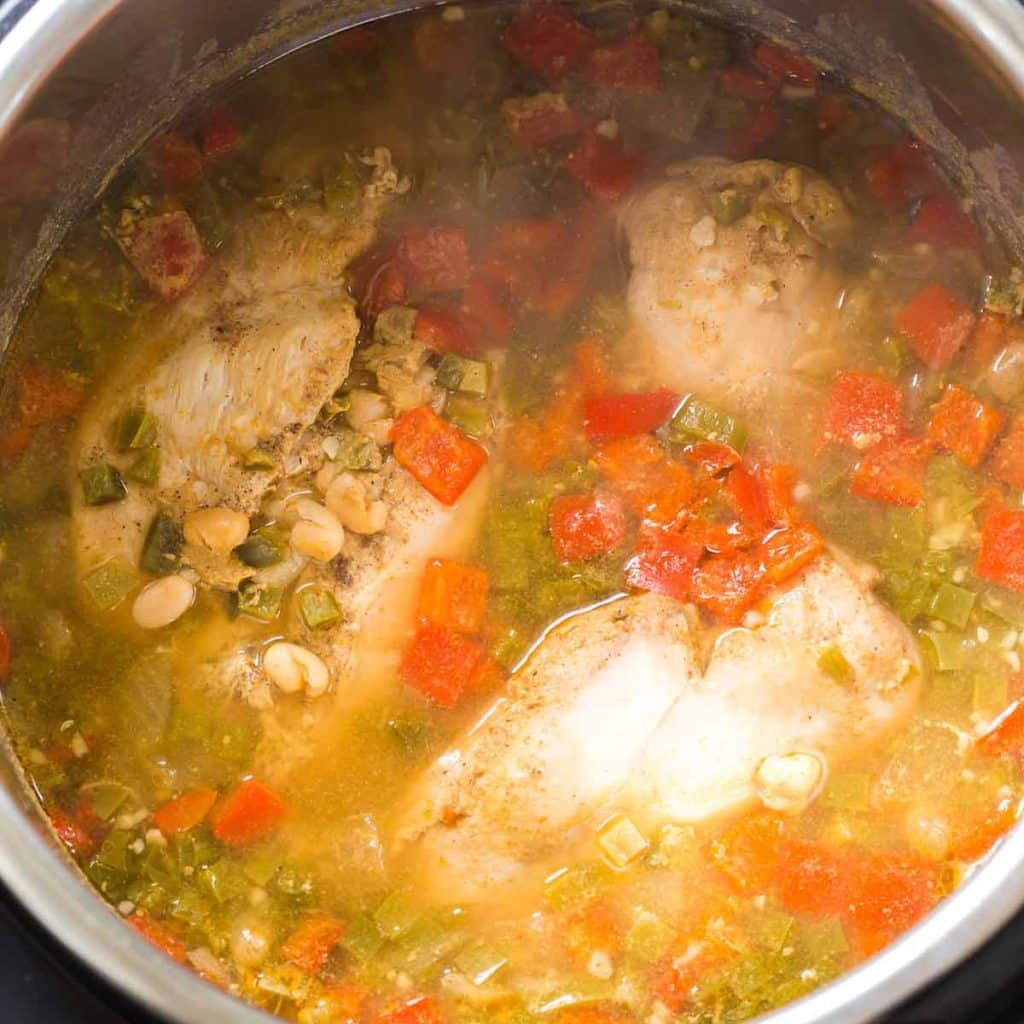 An Instant Pot with a clear broth, cooked chicken breasts, tomatoes and chiles.