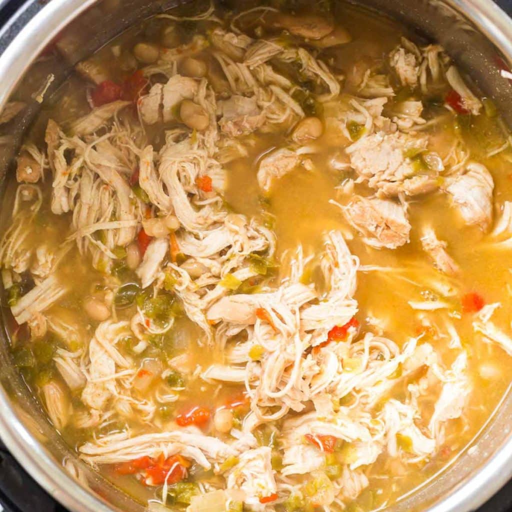 An Instant Pot with cooked shredded chicken, white beans, tomatoes and a broth.
