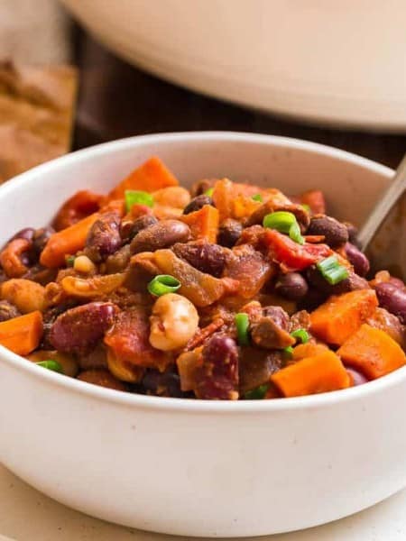 white bowl full of vegan chili, fresh bread in the background