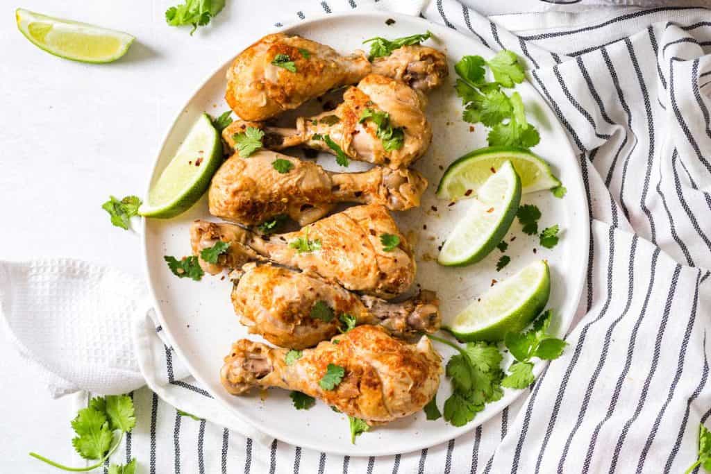 white circular plate with cooked chicken drumsticks topped with chopped cilantro and lime wedges.
