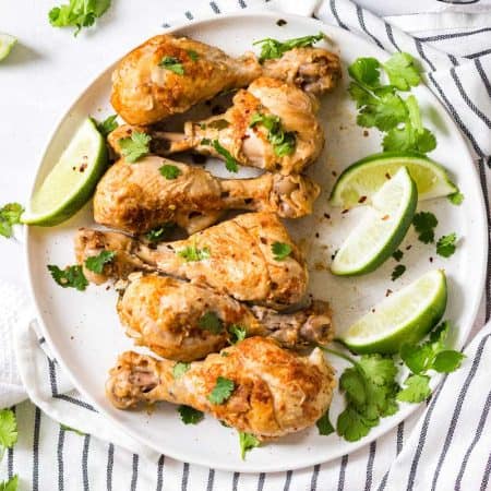 white circular plate with cooked chicken drumsticks topped with chopped cilantro and lime wedges.