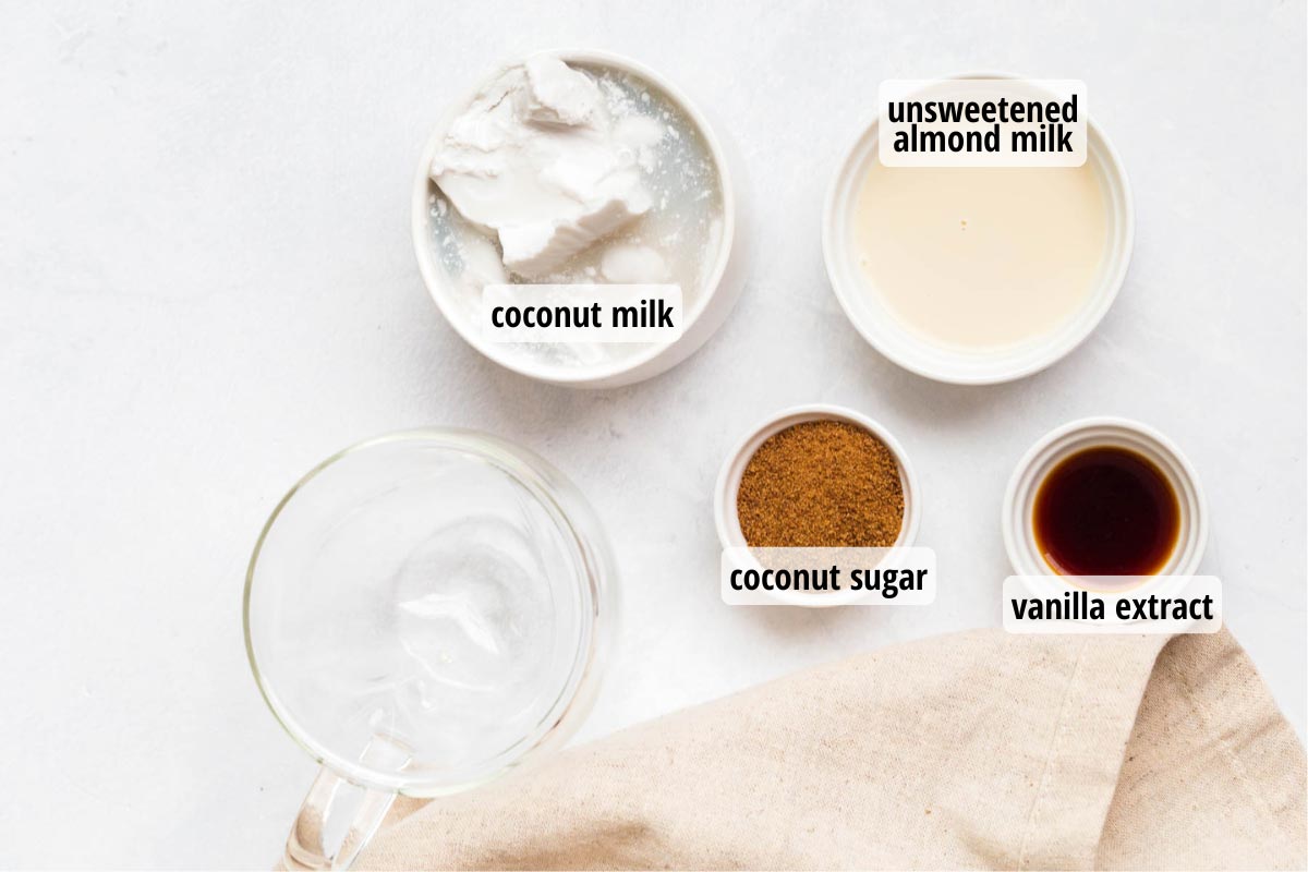 White countertop with clear and white bowls full of coconut milk, almond milk, coconut sugar, and vanilla extract.