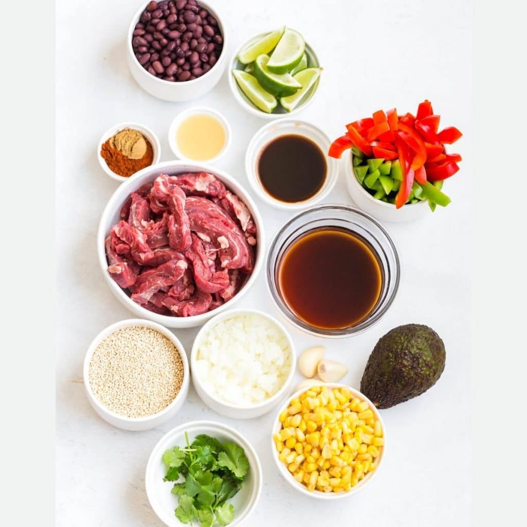 A white counter with 12 bowls full of ingredients to make Steak Fajita Bowls.