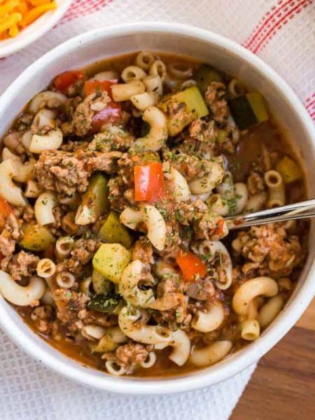 white bowl with goulash on top of a white and red striped napkin.