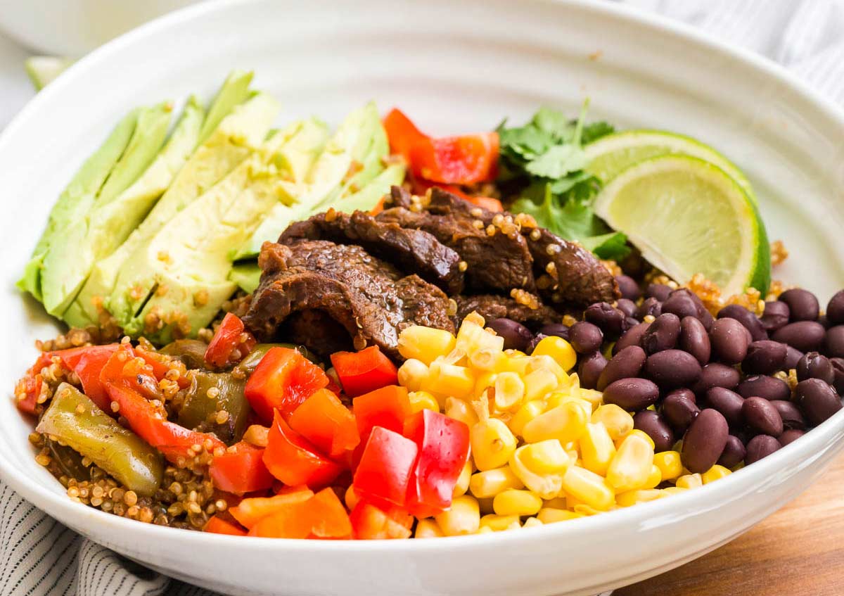 White bowl filled with steak fajitas and fresh toppings.