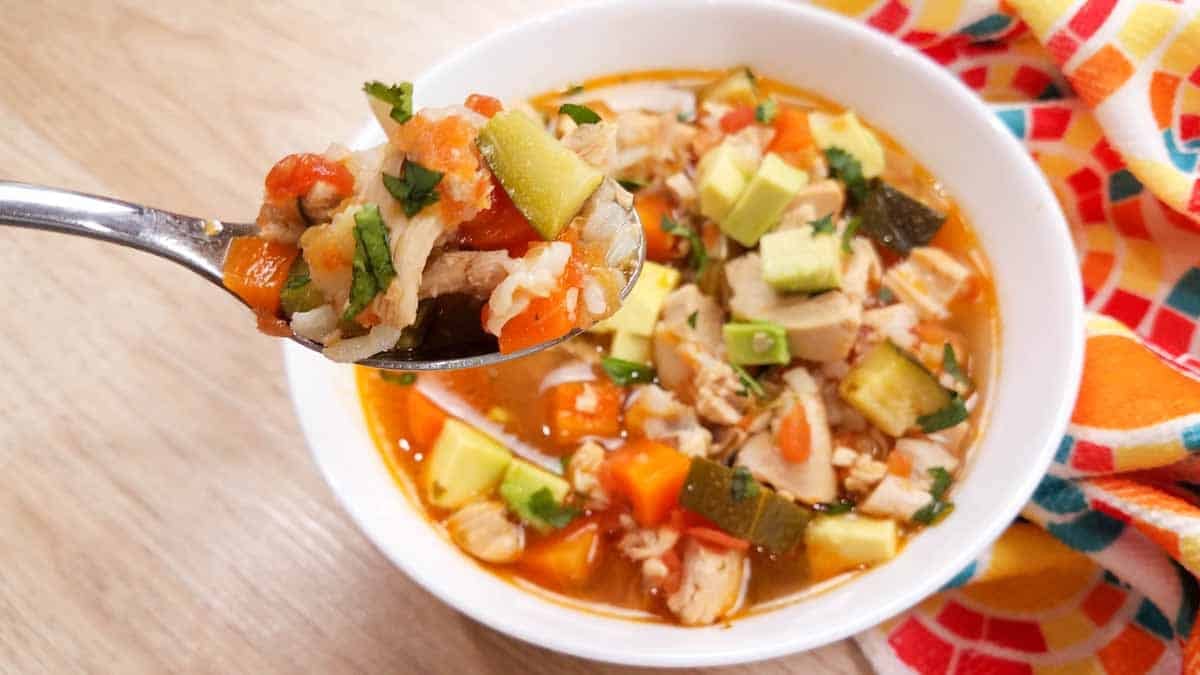 A spoonful of rotisserie chicken soup in the forefront and behind it a white bowl full of rotisserie chicken soup.