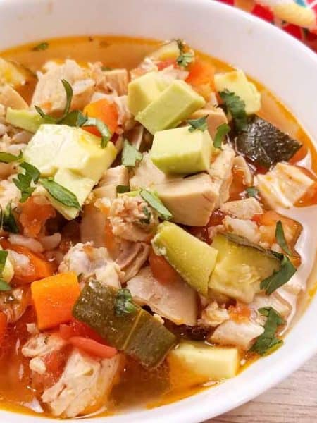 Rotisserie Chicken Soup in a white bowl with a spoon on top of a table with a colorful napkin.