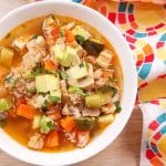 A white bowl full of rotisserie chicken soup on a wood table with a colorful napkin off to the side.