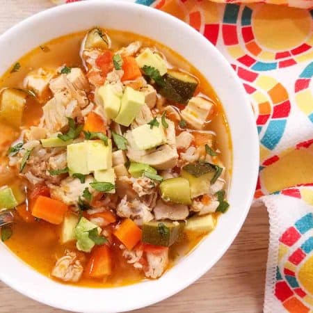 A white bowl full of rotisserie chicken soup on a wood table with a colorful napkin off to the side.