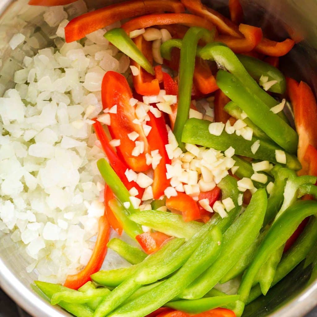 Inside of an Instant Pot showing chopped onion, sliced bell peppers, and diced garlic ready to be cooked.