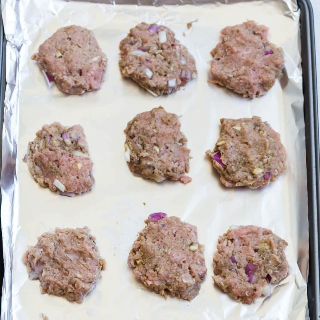 Nine uncooked turkey sausage patties on a foil lined baking sheet.