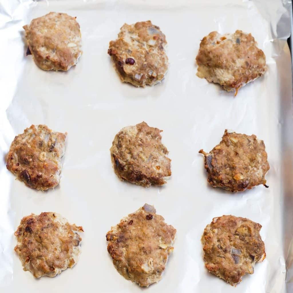 Nine cooked turkey sausage patties on a foil lined baking sheet.