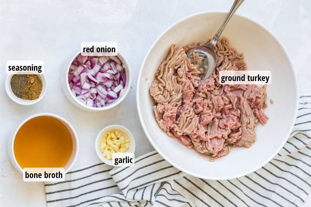 A marbled counter top with white bowls full of different labeled ingredients needed to make turkey sausage.
