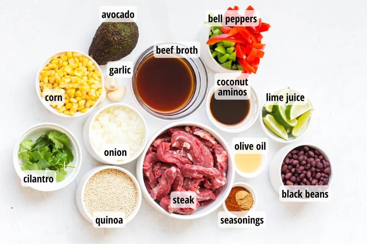 A white counter with 12 bowls, all labeled, full of ingredients to make Steak Fajita Bowls.