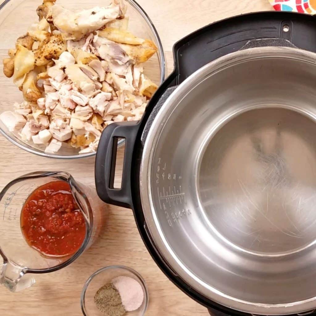 An empty Instant Pot with a bowl of cut up chicken pieces off to the side.