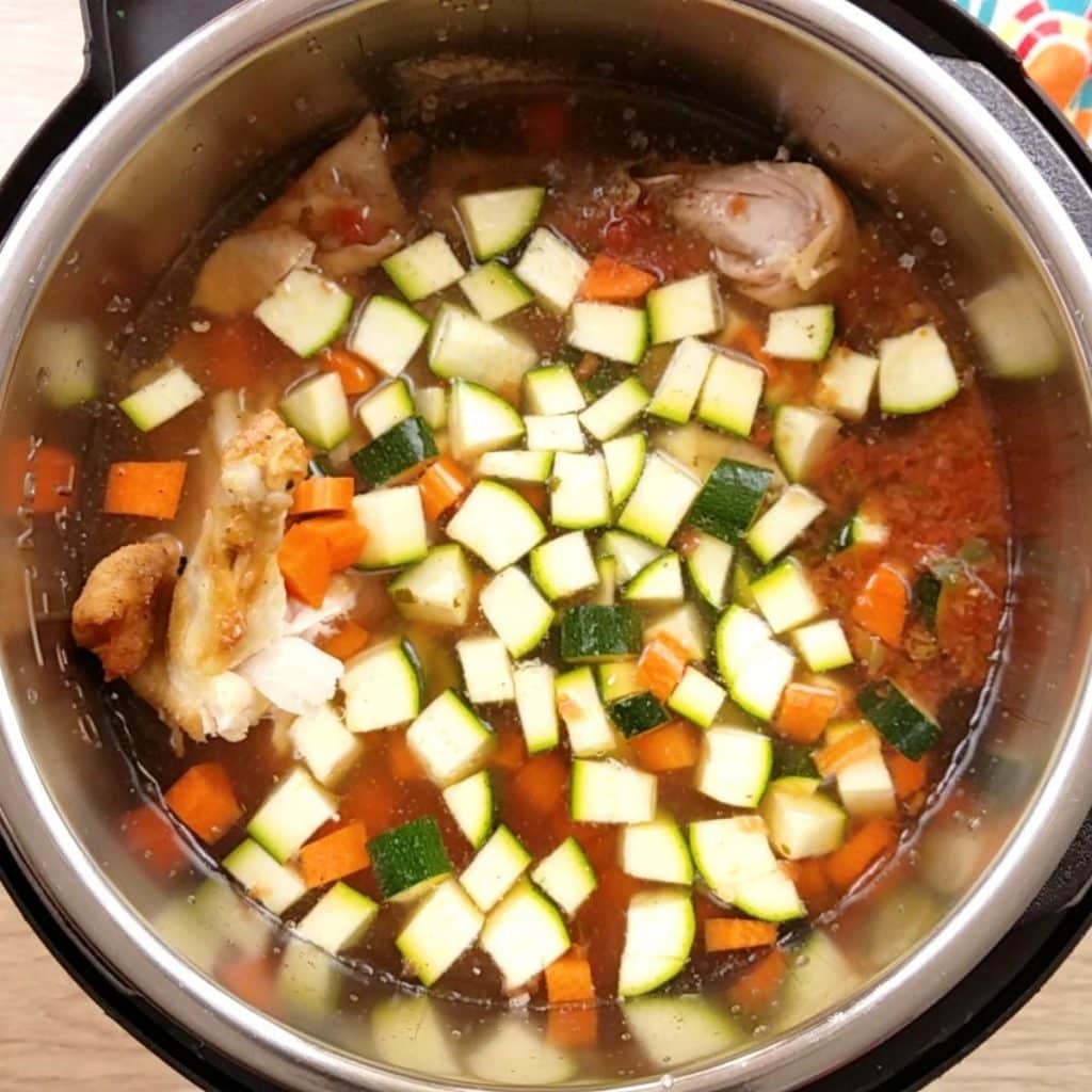 An Instant Pot filled chicken chicken, diced zucchini and carrots and other seasonings.