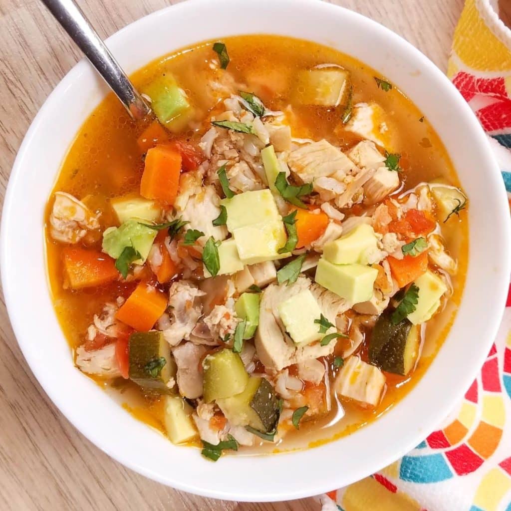 A white bowl with a spoon in it filled with rotisserie chicken soup.