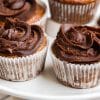 Banana Cupcakes with Chocolate Peanut Butter Frosting in paper liners on top of a white cakestand