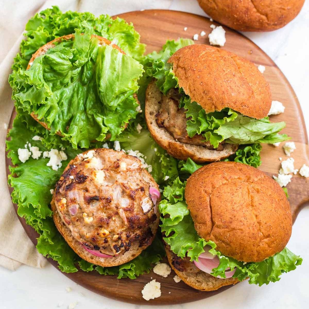 three turkey burgers on a wood plater. Two burgers have buns, one does not. Lettuce on the wood platter as well.