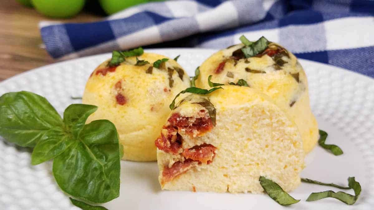 A white plate with three cooked egg bites and a sprig of basil.