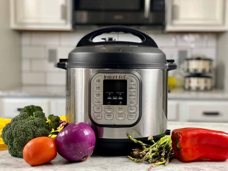 Instant Pot pressure cooker on w white marble counter with fresh vegetables around it.
