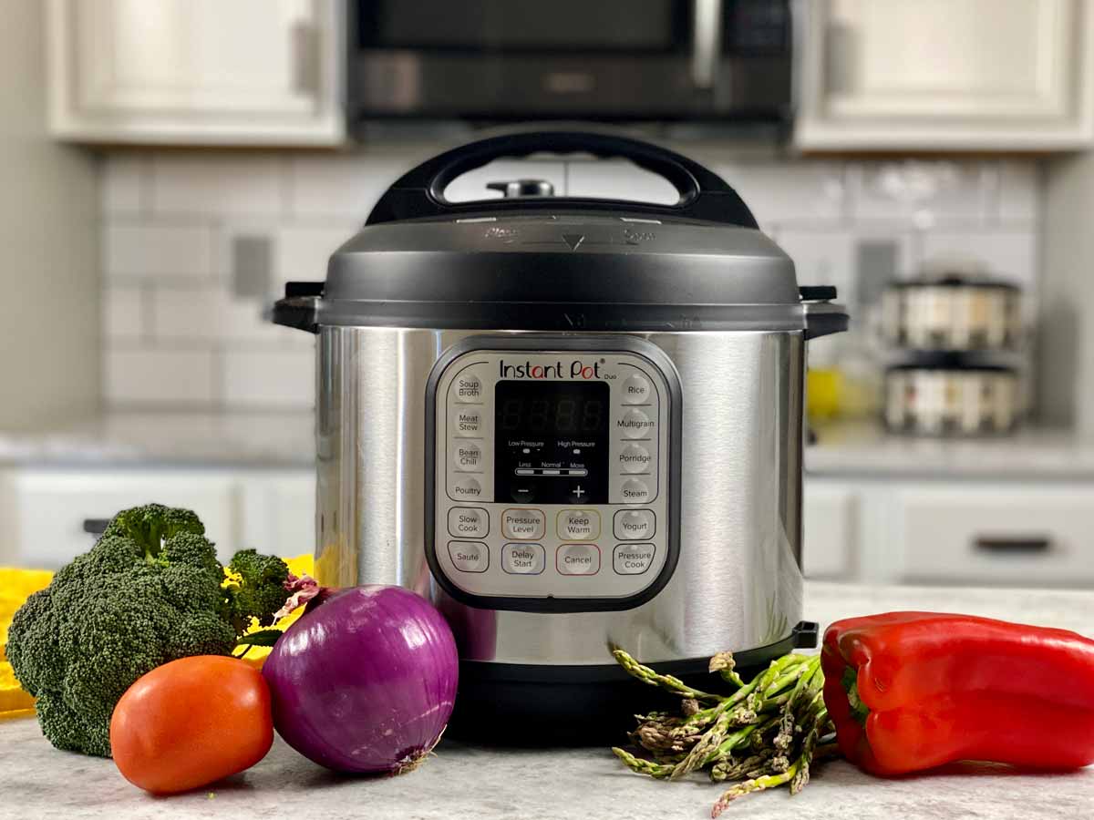 Instant Pot pressure cooker on w white marble counter with fresh vegetables around it.