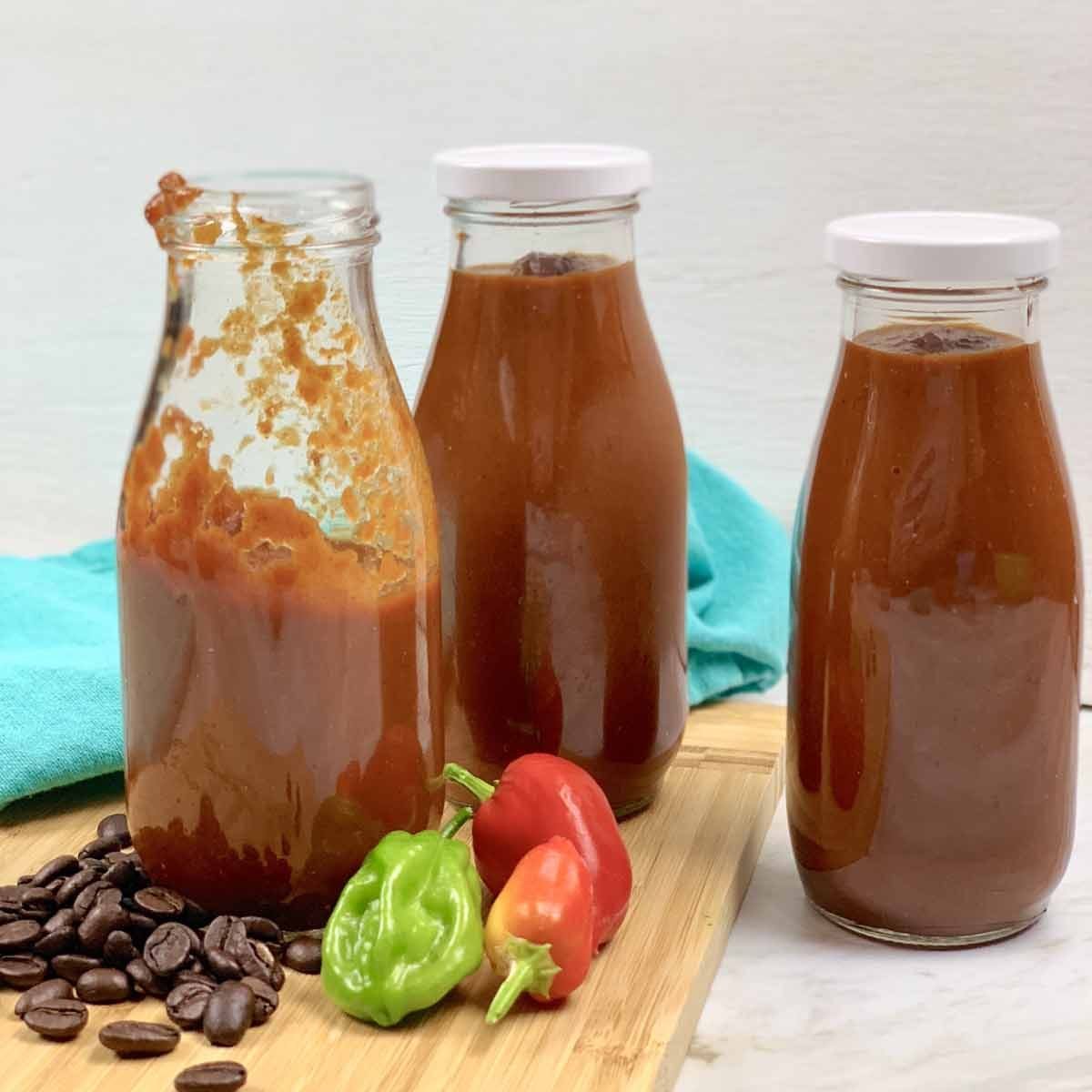 three jars of BBQ Sauce, two with white tops. On the counter are coffee beans and hot peppers.