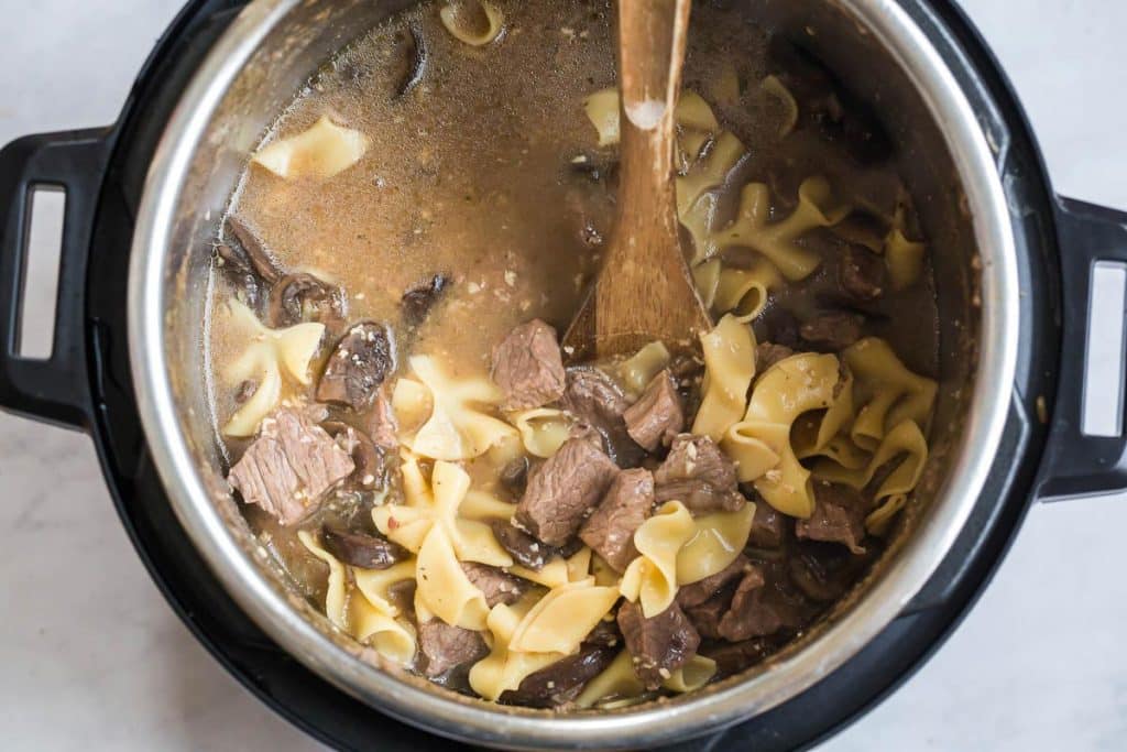 instant pot with noodles, beef and mushroom sauce being stirred with a wooden spoon