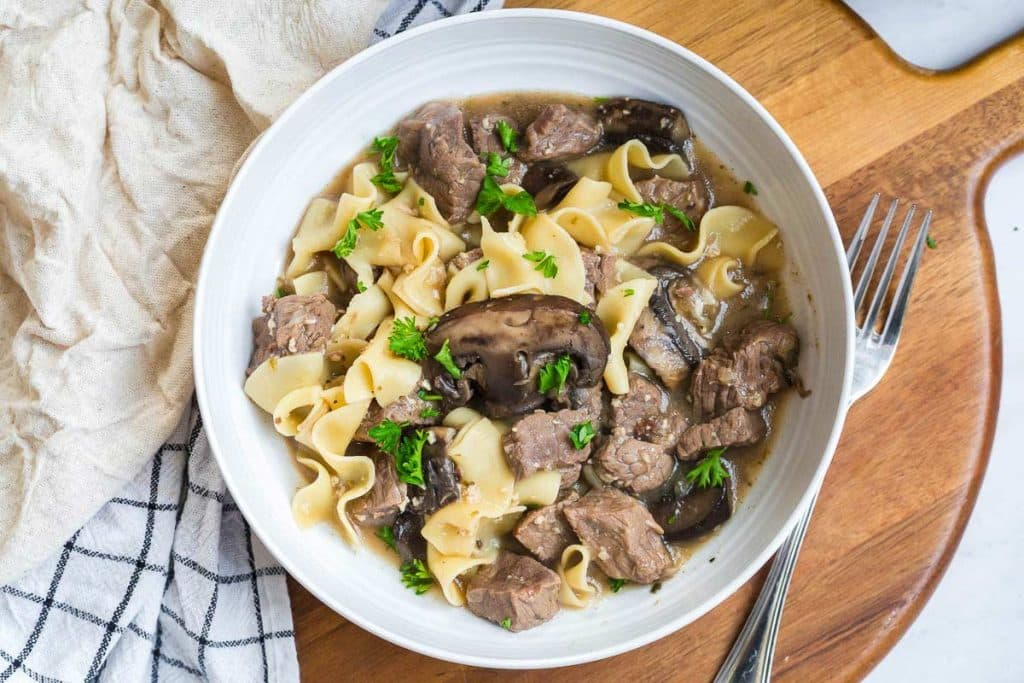 white bowl full of noodles, beef, mushrooms and stroganoff sauce.