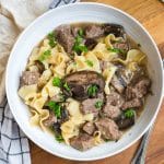 white bowl full of noodles, beef, mushrooms and stroganoff sauce.