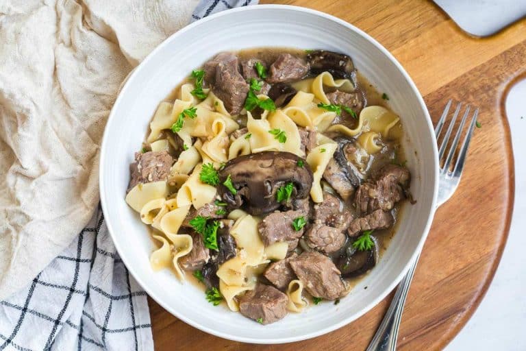 white bowl full of noodles, beef, mushrooms and stroganoff sauce.