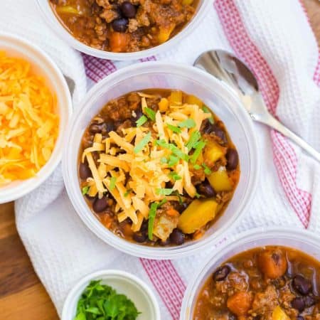 view of sweet potato chili topped with cheese from above on top of a white and red napkin with shredded cheese and a spoon to either side