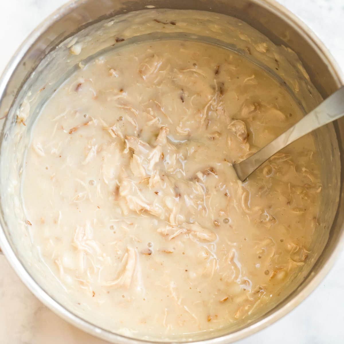 A large pot full of creamy soup showing shredded chicken mixed in.
