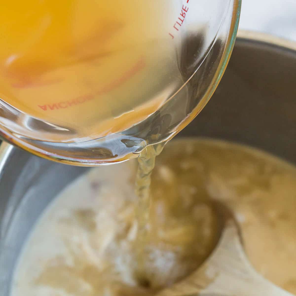 Chicken broth being poured out of a measuring cup into a pot to make cream of chicken soup.