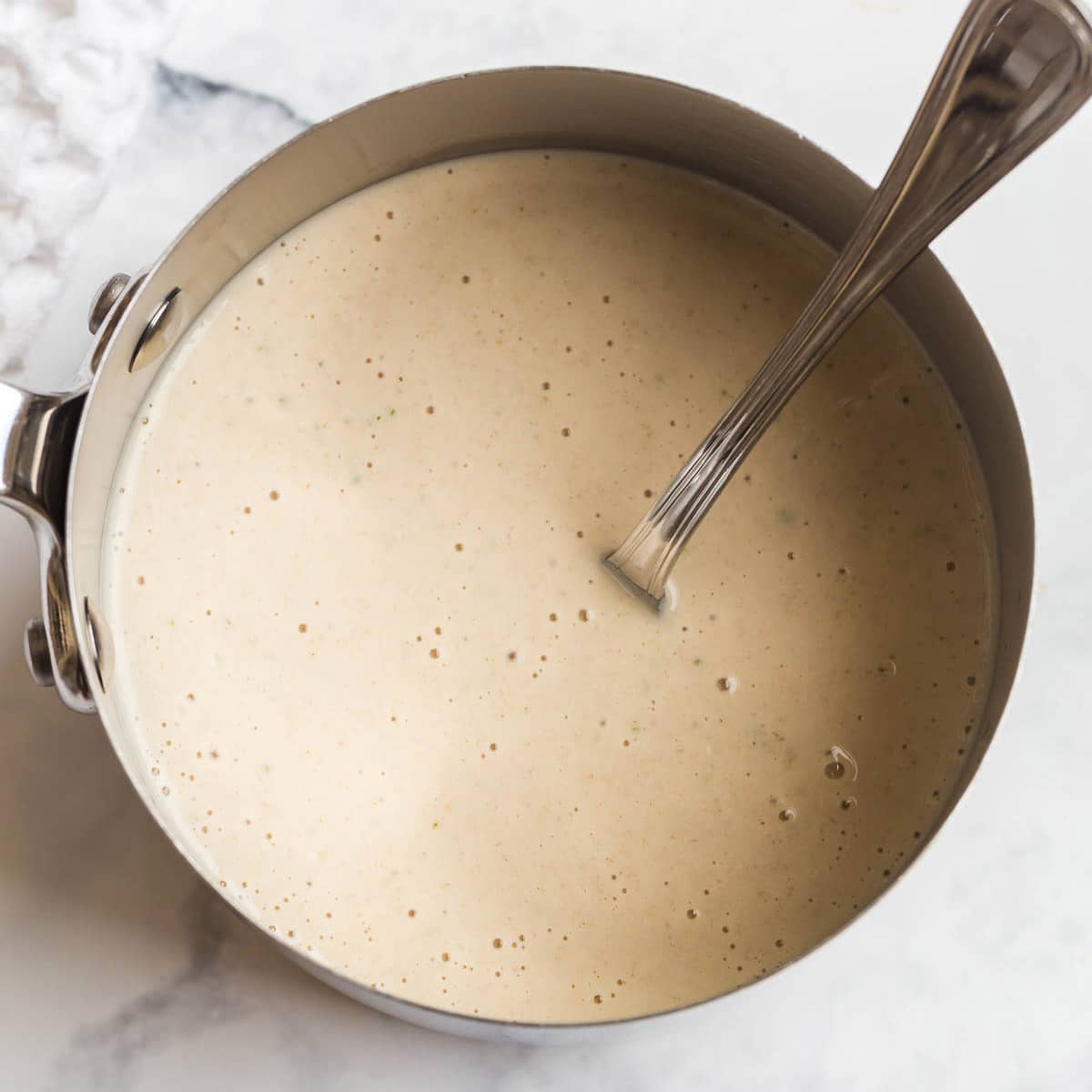 A pot with a large spoon stirring almond milk and broth for cream of chicken soup.