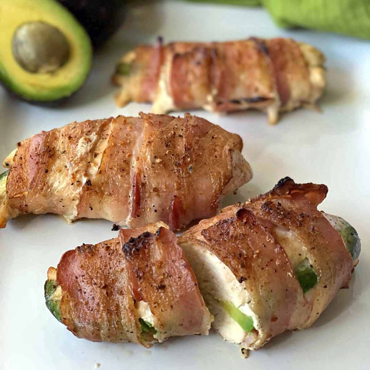 Three pieces of chicken that have been stuffed with avocado and wrapped in bacon and then grilled.