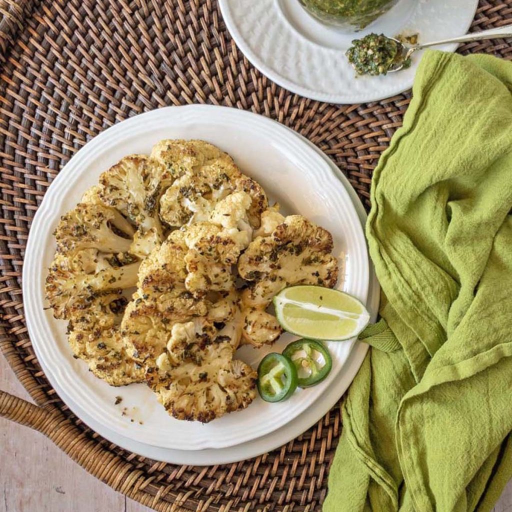 Cauliflower steaks with lime and jalapeno on a white plate with a green napkin off to the right.