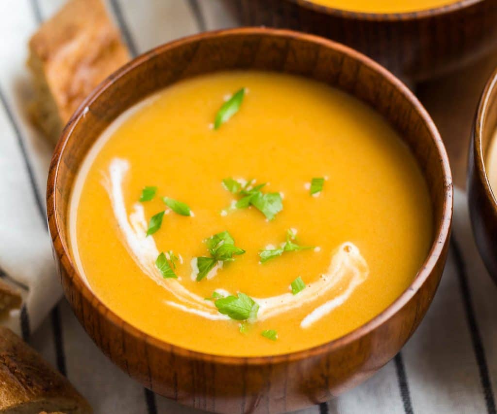 wooden bowl with creamy butternut squash soup and a drizzle of cream and sprinkle of parsley