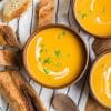 three wooden bowls with creamy butternut squash soup and a drizzle of cream and sprinkle of parsley