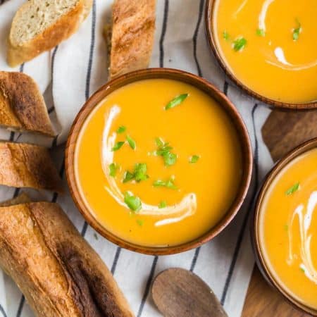 three wooden bowls with creamy butternut squash soup and a drizzle of cream and sprinkle of parsley